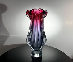 a pink and purple glass vase sitting on top of a black table next to a white wall