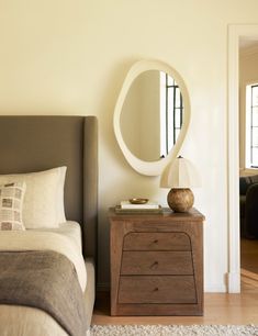 a bedroom with a bed, night stand and large round mirror on the wall above it