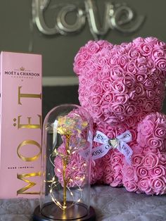 a pink teddy bear sitting next to a box and a rose in a glass case