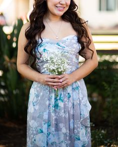 a woman in a blue dress holding a bouquet of flowers and smiling at the camera