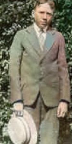 a man wearing a suit and tie holding a white object in front of some bushes