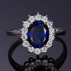 an oval shaped blue sapphire surrounded by smaller round white diamonds on a black ring stand against a gray background