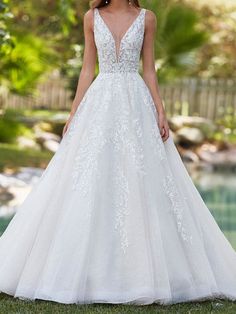 a woman in a white wedding dress standing on the grass near a pool and trees