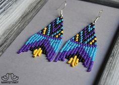 a pair of beaded bird earrings sitting on top of a wooden table next to a frame