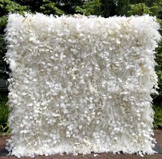 a large white pillow sitting on top of a brick floor next to bushes and trees