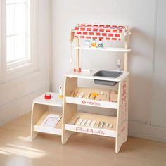 a wooden toy kitchen set sitting on top of a hard wood floor next to a window