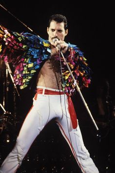 a man in white pants holding a microphone and wearing a colorful jacket on top of his shoulders