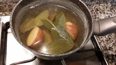 a pot filled with green leaves and apples on top of a stove burner next to an oven