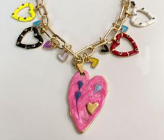 This one-of-a-kind heart necklace is colorful and whimsical. Five colorful hearts and eight mini hearts dangle from a gold tone paperclip link chain. The center large pink heart measures 1 x 1 3/4". Four more hearts measure approx 3/4" x 3/4". Necklace measures 17" with a 1" extender. Pink Dangle Charm Necklace With Adjustable Chain, Dangle Heart Charm Necklace, Valentine's Day Dangling Charms Necklaces, Valentine's Day Dangle Necklaces With Charms, Valentine's Day Necklace With Dangling Charms, Whimsical Gold Necklace For Valentine's Day, Whimsical Gold Heart Necklace, Pink Heart Pendant Charm Necklace With Lobster Clasp, Pink Heart-shaped Charm Necklaces With Lobster Clasp