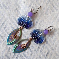 Jewel toned earrings featuring green, blue and purple leaf shaped enameled charms with gold details. They are topped with ruffled blue lampwork beads, sterling beads and purple quartz beads. Simple copper swirls dangle from the center. These stylish earrings measure 3 3/8 inches in total length and hang on niobium earring hooks. Return to shop: bstrung.etsy.com More links where you can find me: Facebook: http://www.facebook.com/bstrung Pinterest: http://pinterest.com/bstrung Instagram: https://w Whimsical Blue Nickel-free Earrings, Handmade Blue Whimsical Flower Earrings, Whimsical Handmade Blue Flower Earrings, Artsy Blue Metal Jewelry, Unique Purple Flower Earrings, Whimsical Nickel-free Purple Earrings, Whimsical Purple Nickel-free Earrings, Nickel-free Purple Enamel Jewelry, Unique Hand Painted Purple Earrings