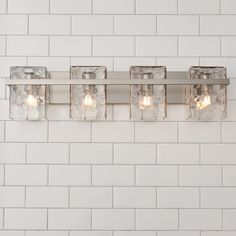 a bathroom light that has four lights on the side of it and is next to a white brick wall