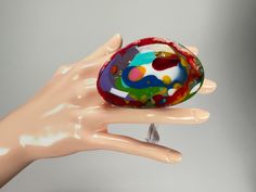 a hand holding a colorful glass object in it's palm on a gray background