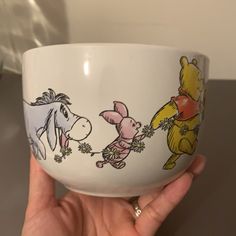 a hand holding a white cup with winnie the pooh and friends painted on it