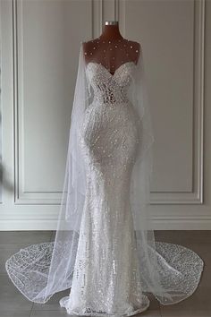 a wedding dress on display in front of a white wall with a veil over it