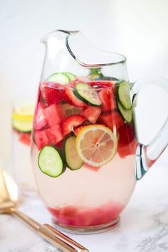 a pitcher filled with watermelon, cucumber and lemon slices next to a spoon