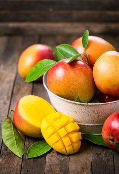 a bowl filled with mangoes and other fruit on top of a wooden table next to leaves