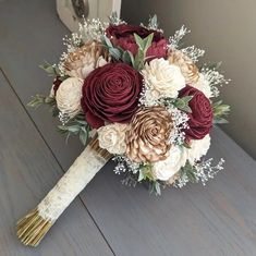 a bridal bouquet with red and white flowers on a wooden table in front of a door