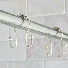 three hooks are hanging from the side of a metal rail with white brick walls in the background