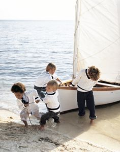 four children are playing on the beach near a sailboat