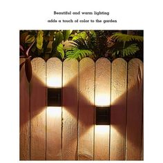 two lights that are on the side of a wooden fence with plants behind them and text reading, beautiful cloud warm lighting adds a touch to the garden