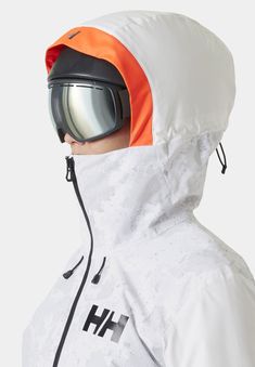 a man wearing an orange and white jacket with ski goggles on his head, looking off to the side