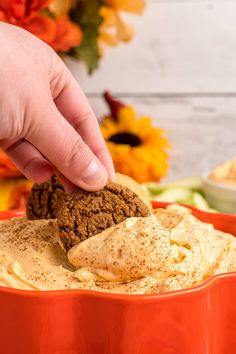 a hand dipping an oreo cookie into a bowl of hummus and pumpkins