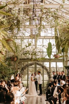 a bride and groom standing in front of an audience at a wedding ceremony with greenery on the walls