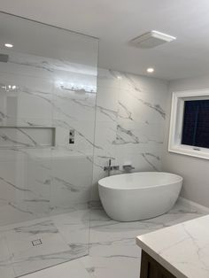 a large white bath tub sitting next to a window in a bathroom with marble flooring