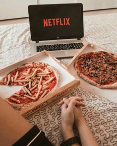 two pizzas sitting on top of a table next to a laptop and a persons hand