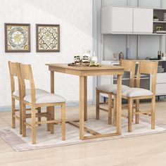 a kitchen table and chairs in front of a white wall with pictures on the wall