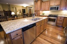 a kitchen with wooden floors and granite counter tops, stainless steel dishwasher on the center island