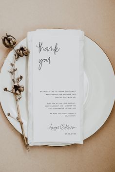 a white plate topped with a piece of paper next to a dried flower on top of a table