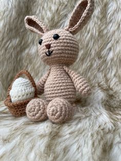 a crocheted bunny sitting next to an egg in a basket on a furry surface