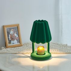 a green lamp sitting on top of a white table next to a framed photo and a candle