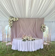 a table with flowers on it under a white drape covered tent for an event