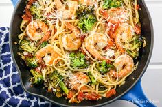 a skillet filled with pasta and shrimp on top of a blue towel next to a wooden spoon