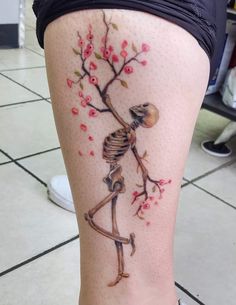 a woman's leg with a skeleton and cherry blossom tree tattoo on her thigh