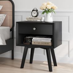 a night stand with books and a clock on the side table next to a bed