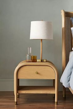 a wooden night stand next to a bed with a white lamp on top of it