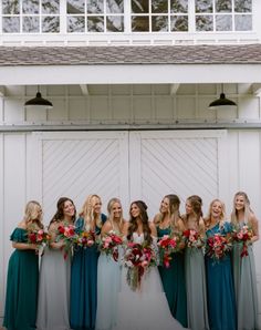 a group of women standing next to each other in front of a white building holding bouquets