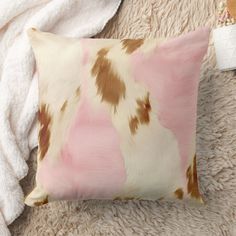 a pink and brown pillow sitting on top of a fluffy white rug next to a blanket