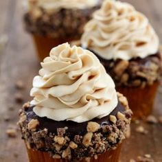 three cupcakes with white frosting and walnuts on the top are sitting on a wooden table