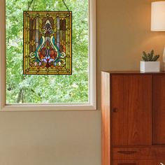 a stained glass window hanging from the side of a wall next to a wooden dresser