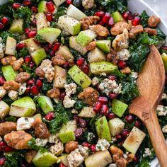 a salad with apples, cranberries and walnuts in a white bowl next to a wooden spoon