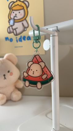 a teddy bear sitting next to a keychain on a desk with a sign in the background