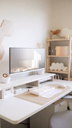 a white desk with a computer monitor and keyboard sitting on it's side in front of a book shelf