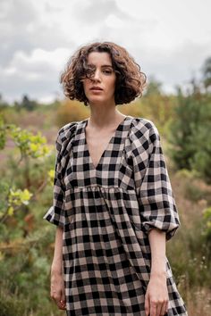 a woman wearing a black and white checkered dress standing in the grass with her hands on her hips