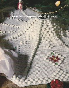 a crocheted christmas tree skirt with poinsettis on it and presents under the tree