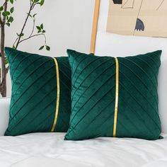 two green pillows sitting on top of a white bed next to a potted plant