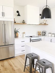 two stools are in front of the kitchen counter and refrigerator, which is white with black accents